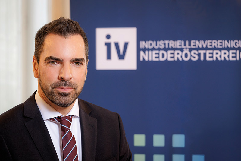Kari Ochsner vor Logo Industriellenvereinigung NÖ