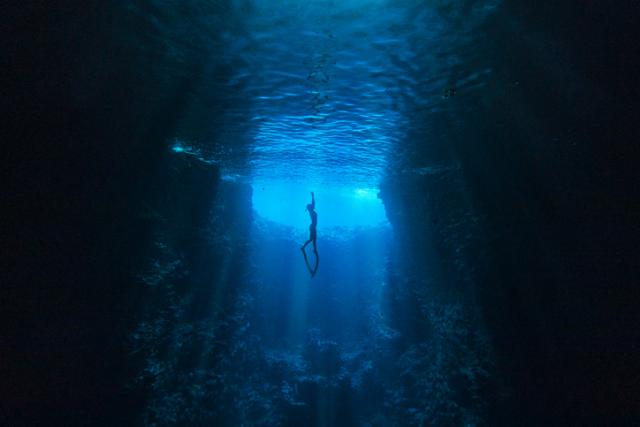 Taucher schwimmen in Unterwasserhöhle in Richtung des Lichts an der Meeresoberfläche