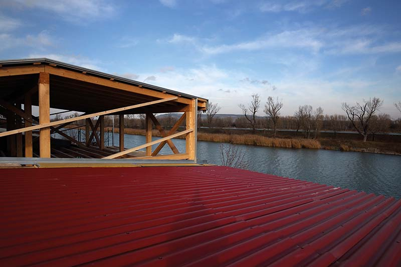 Foto: Für die Dach- und Wandabdeckung des Holzbaus kommen rote Eternit-Wellplatten zum Einsatz.
