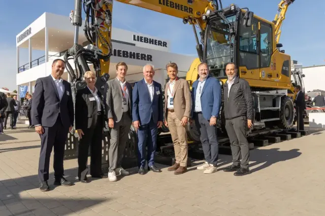 Gruppenfoto vor einem neuen Zweiwegebagger
