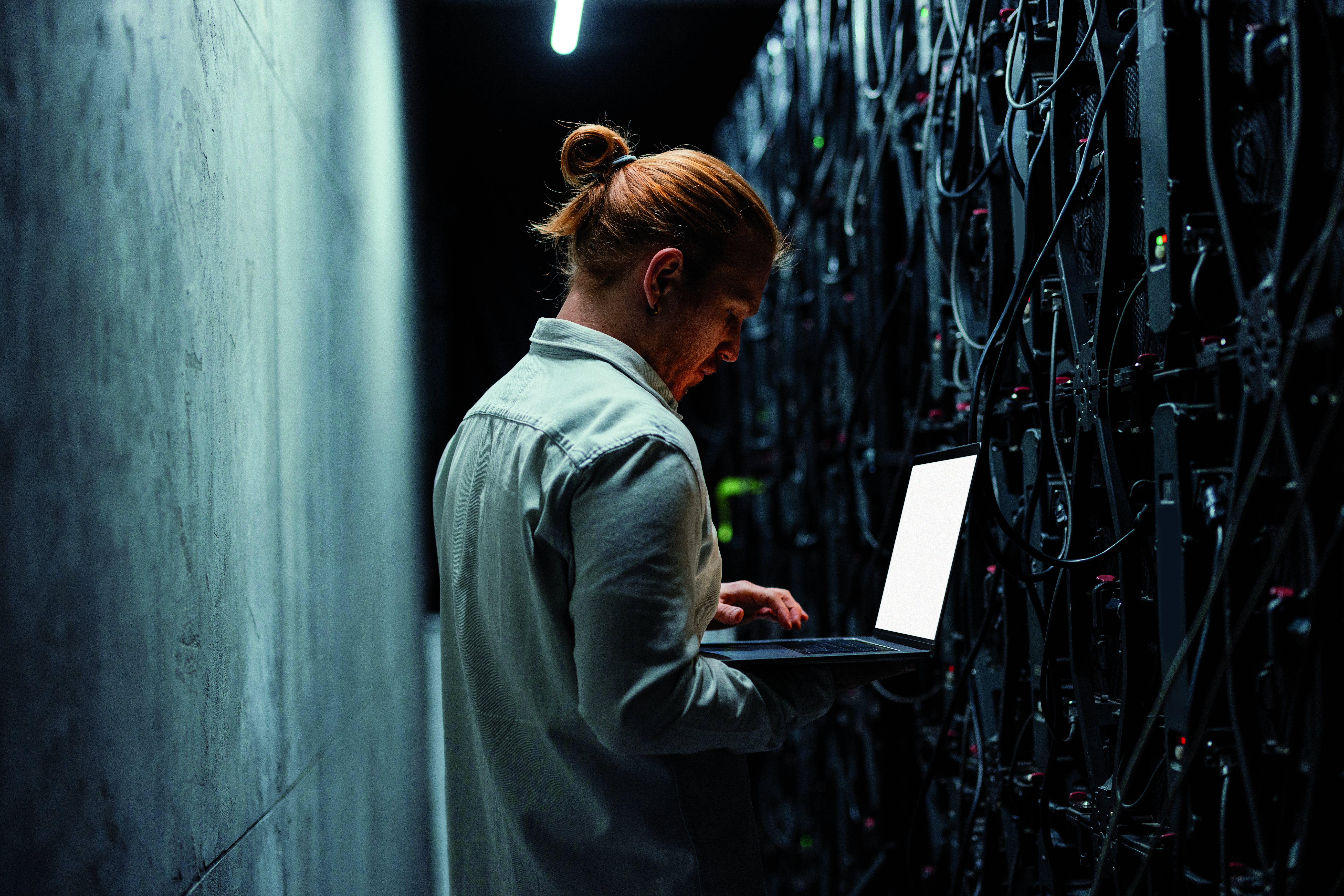 Mann mit Laptop vor Serverwand