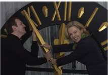 Eric Adler und Michaela Reitterer, Betreiberin des Boutiquehotels Stadthalle, vor der Uhr, die fünf vor zwölf anzeigt.
